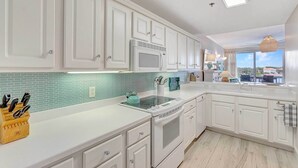 A modern kitchen with white cabinetry, a microwave, a stove, and a backsplash. - Okaloosa Island Escape: Bayfront Condo Near Beach (Fort Walton Beach)