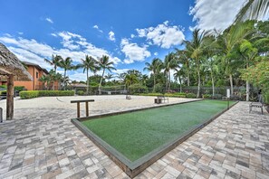 Une cour avec un terrain de croquet, des palmiers et un bâtiment au toit de chaume.