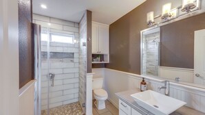 A bathroom with a glass-enclosed shower, a white toilet, a sink, and a mirror with lights above. - Pet-friendly Austin Home w/ Private Yard + Deck! (Austin)