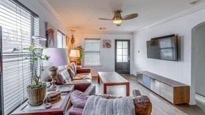 A living room with a sofa, coffee table, and TV. There is a ceiling fan, a potted plant, and a window with blinds. - Pet-friendly Austin Home w/ Private Yard + Deck! (Austin)