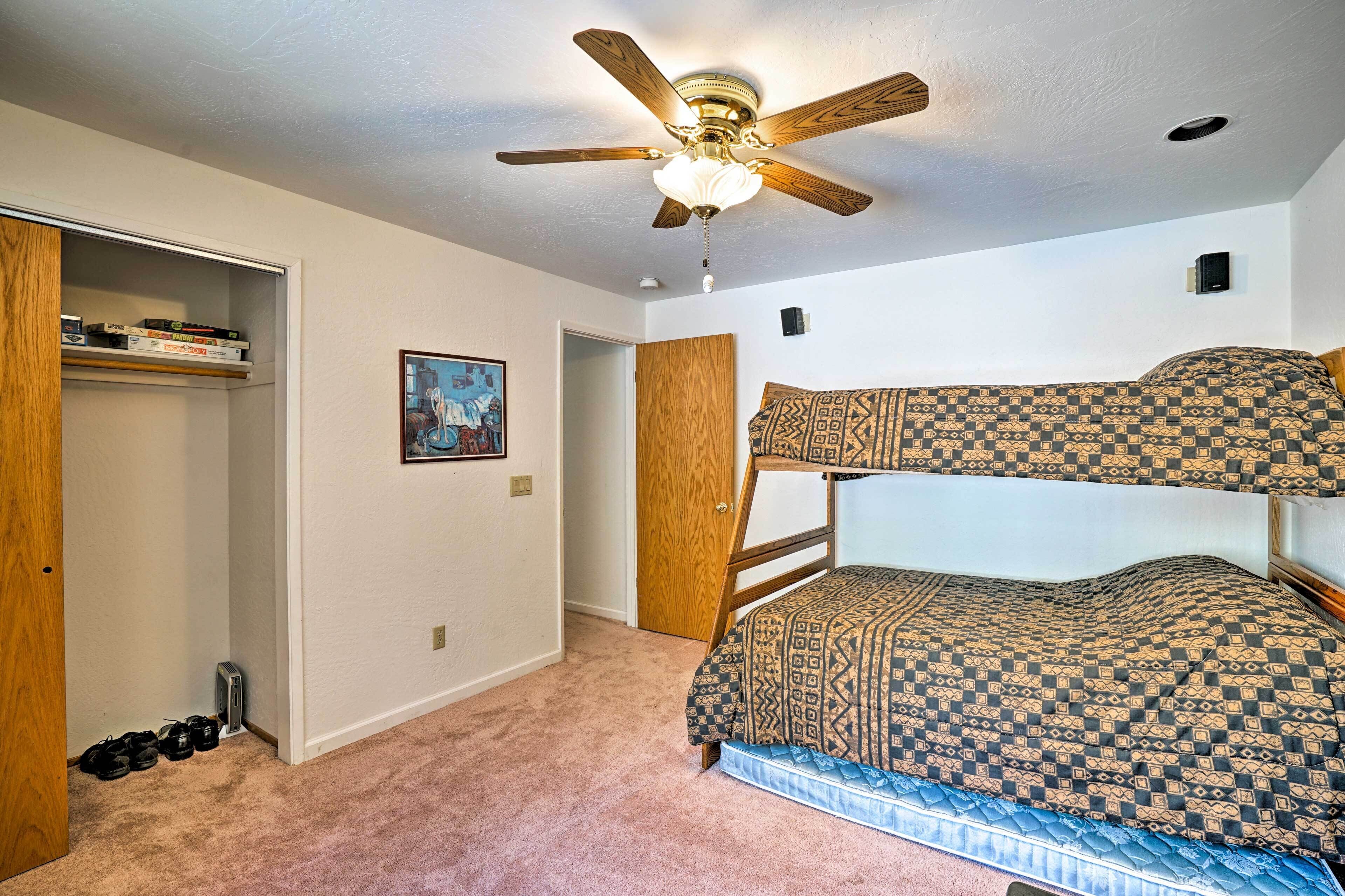 A room with bunk beds, a ceiling fan, a closet, and a door leading to another room.