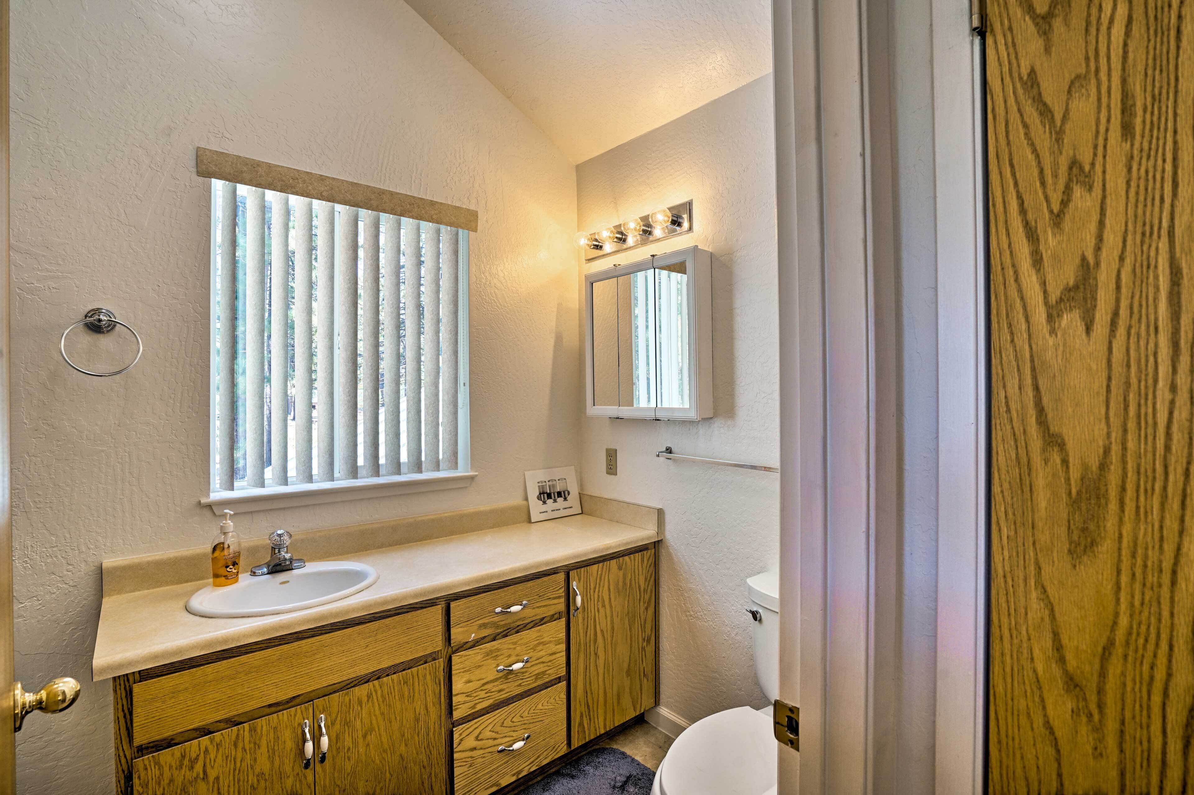 A bathroom with a wooden vanity, a sink, a mirror with lights, and a toilet.