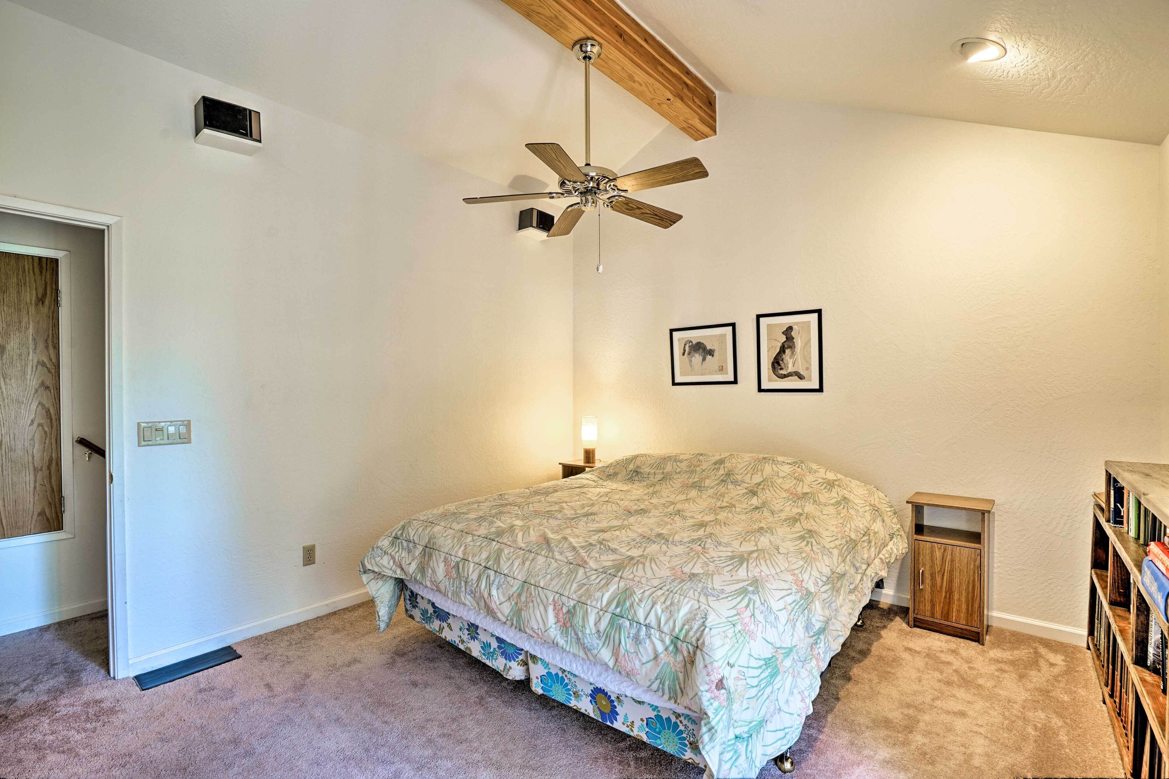 Un dormitorio con cama, ventilador de techo, lámpara de pared y un pequeño armario de madera.