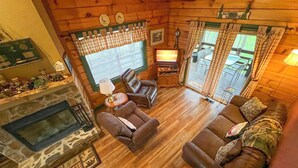 A cozy cabin interior with a fireplace, leather sofas, and a television. - Serene Cabin in the Smokies w/ 2 Decks & Hot Tub! (Waynesville)