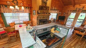 A rustic cabin interior with a kitchen featuring a stove, a dining area with wooden chairs, and a fireplace. - Serene Cabin in the Smokies w/ 2 Decks & Hot Tub! (Waynesville)