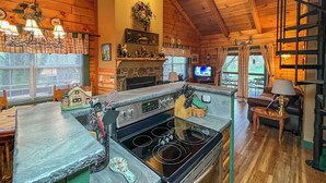 A cozy cabin-style kitchen with a stone fireplace, a large stove, and a dining area with wooden chairs. - Serene Cabin in the Smokies w/ 2 Decks & Hot Tub! (Waynesville)