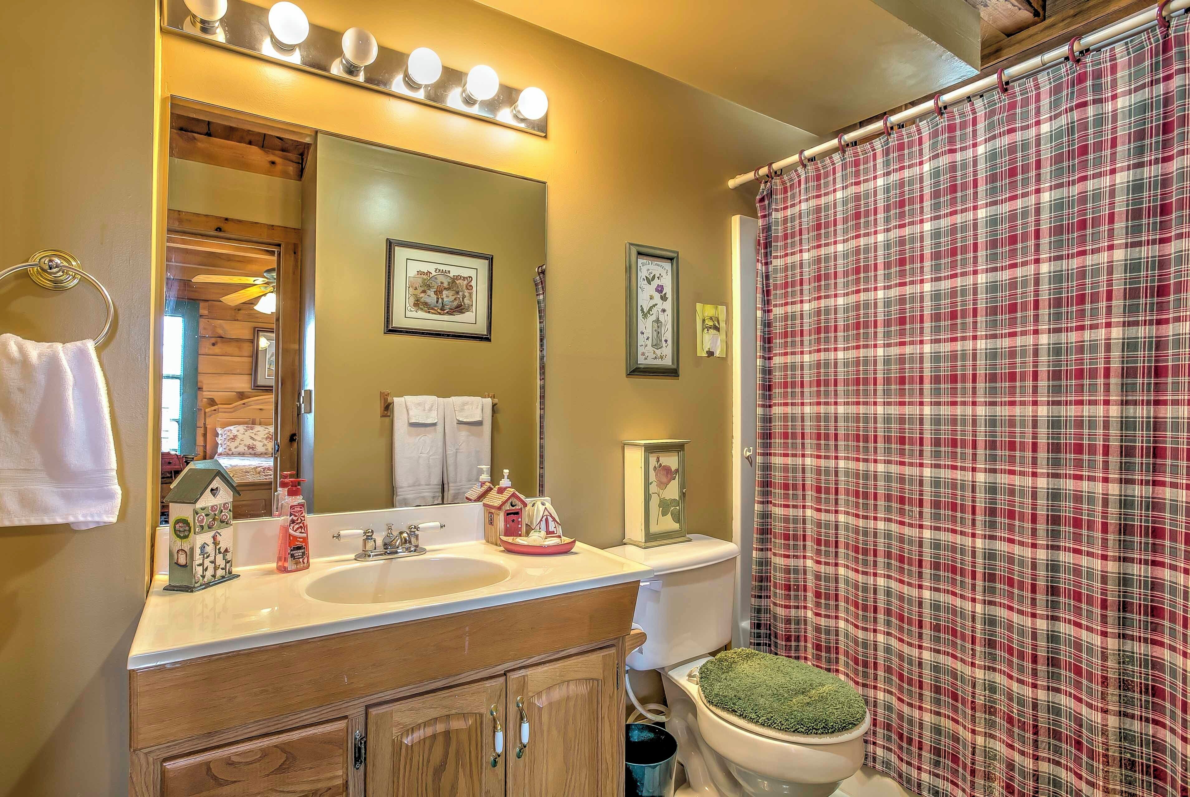 A bathroom with a large mirror, two sinks, a toilet with a green moss top, and a plaid shower curtain.