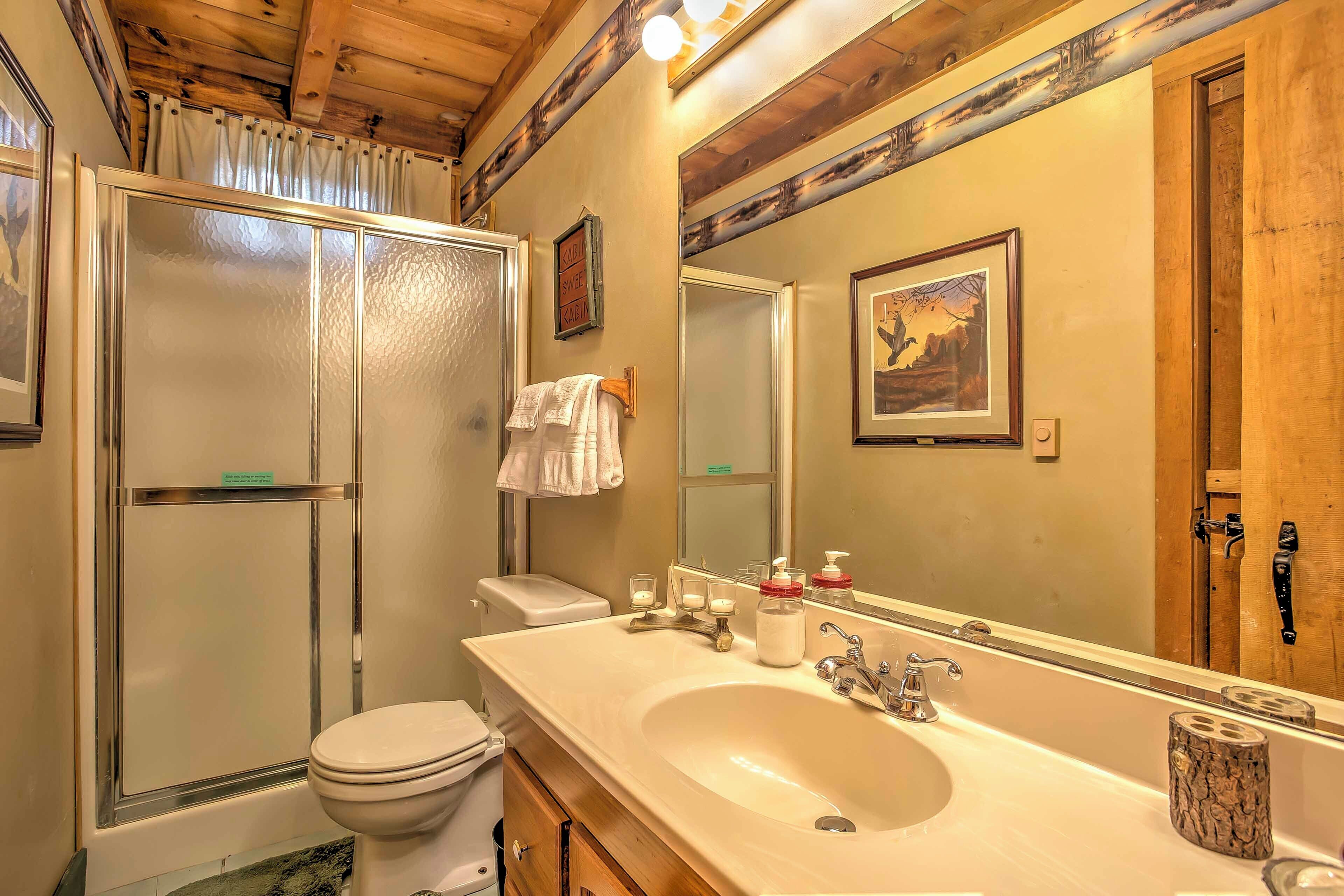 Un baño con cabina de ducha de vidrio, inodoro, lavabo con un espejo grande y techo de madera.