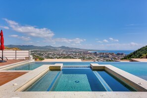 A rooftop infinity pool with a city view, a red umbrella, and a wooden deck.