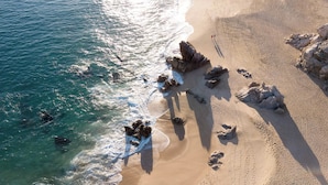 An aerial view of a beach with clear blue waters, rocky formations, and footprints. - Cabo Pedregal Condo: Ocean View & 2 Infinity Pools (Cabo San Lucas)