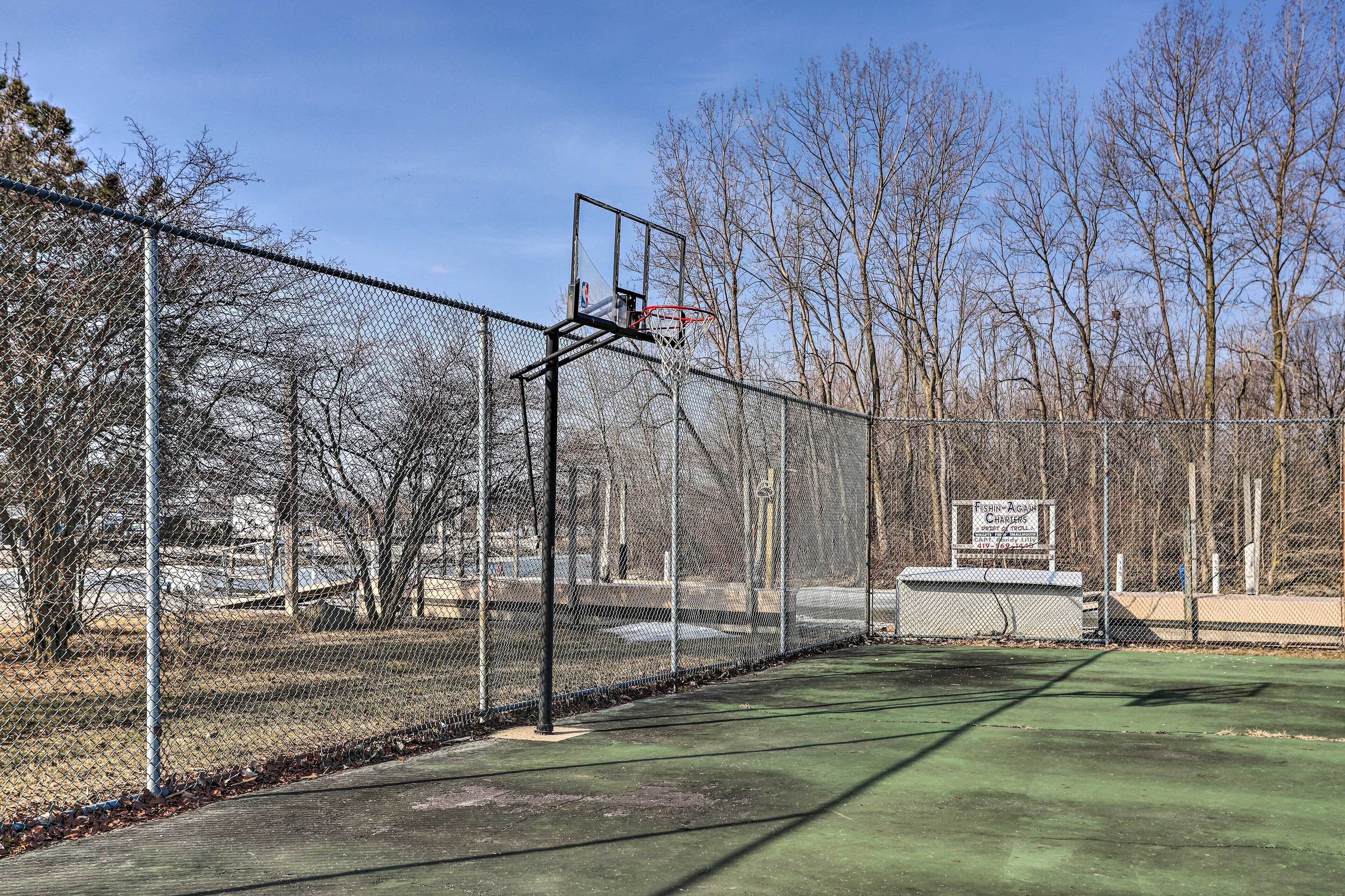 A basketball court with a chain-link fence, a basketball hoop, and a sign indicating a fishing and ice skating area.