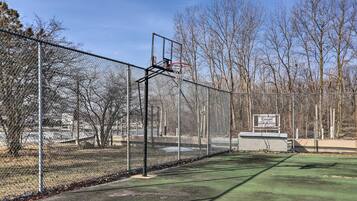 A basketball court with a chain-link fence, a basketball hoop, and a sign indicating a fishing and ice skating area.