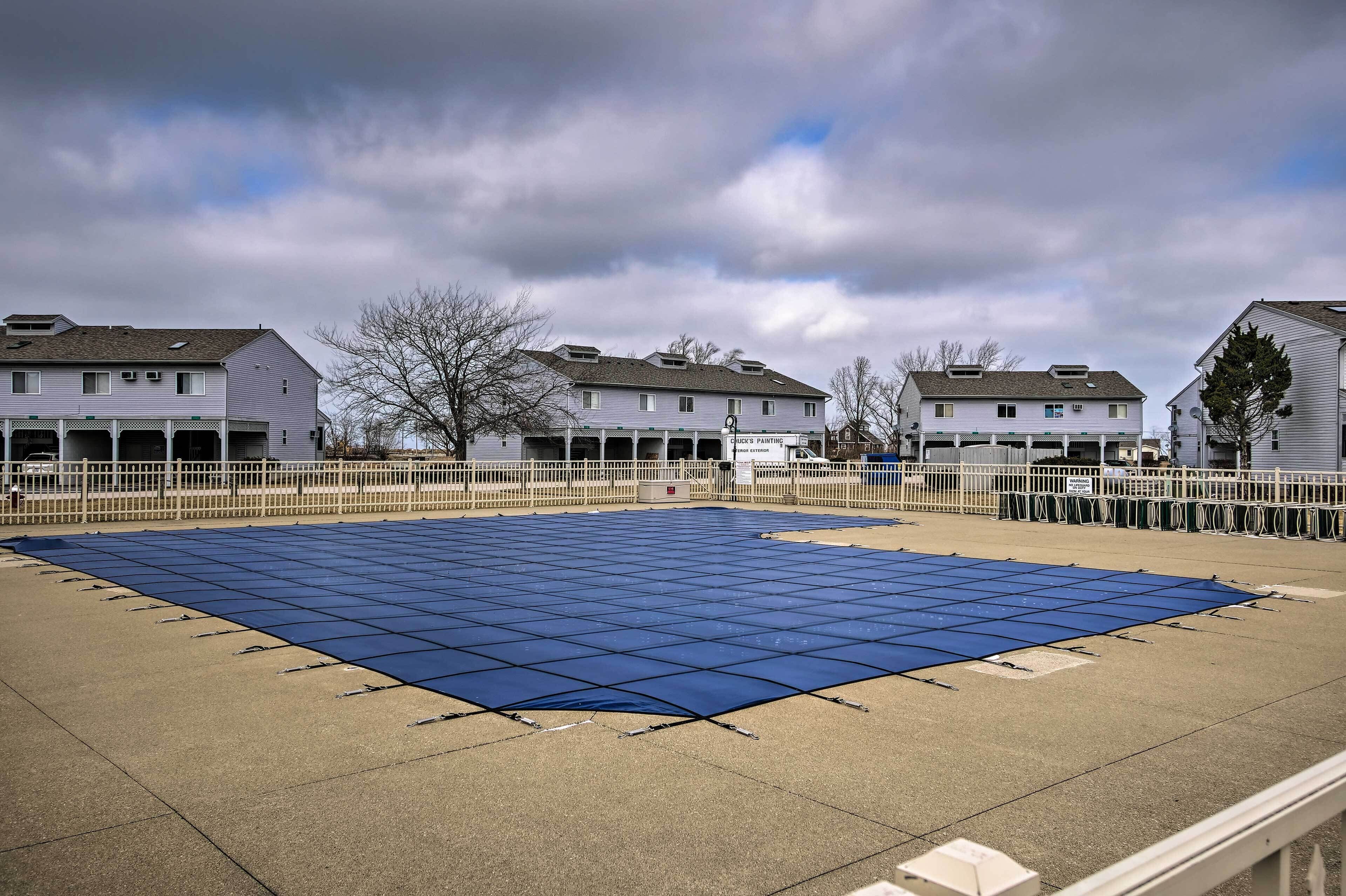 Une vaste zone extérieure avec une bâche bleue recouvrant un sol en béton, entourée d’une clôture blanche et bordée de bâtiments en arrière-plan.
