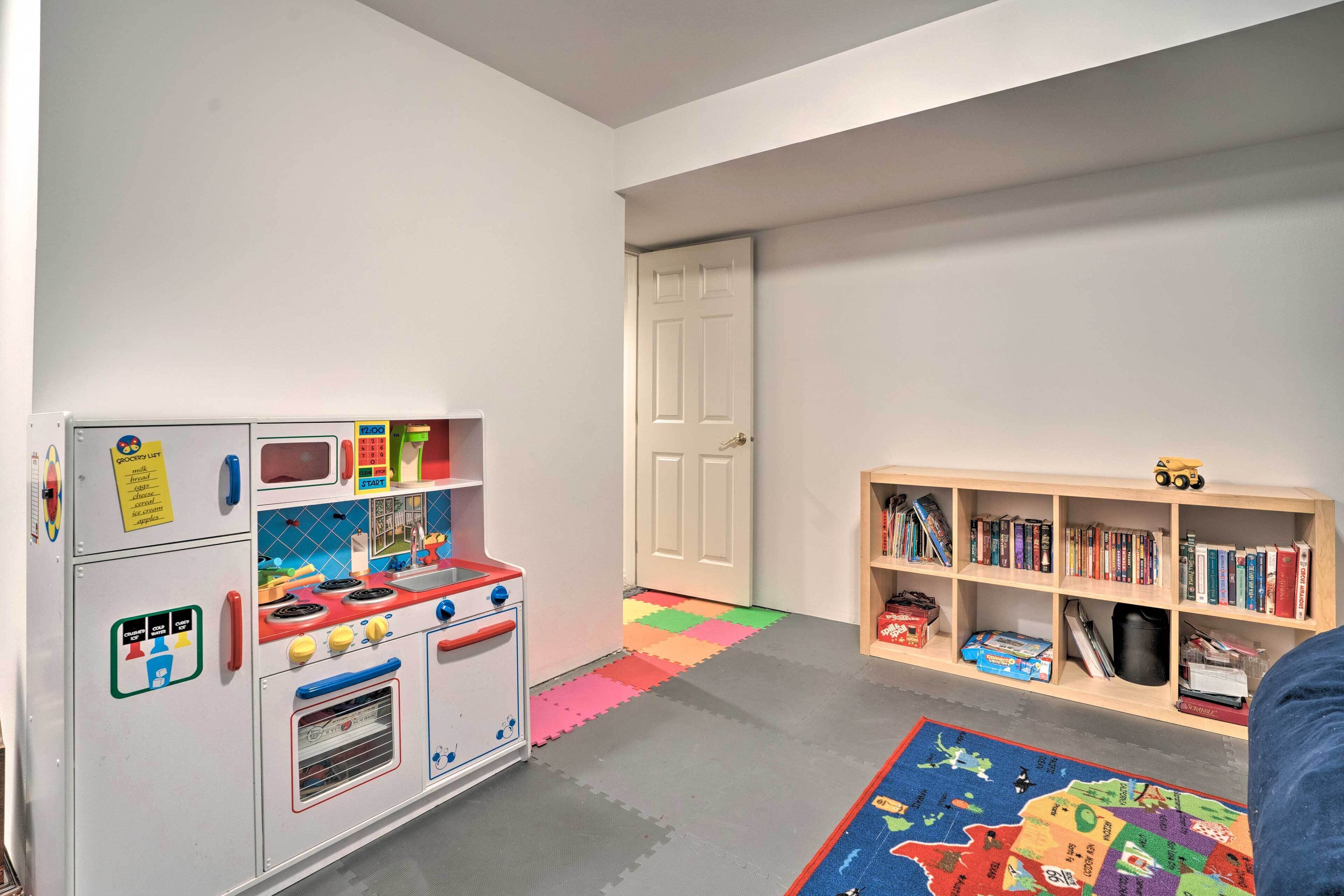 Een kinderspeelruimte met een keukenspeelset, een boekenkast en een kleurrijke mat.