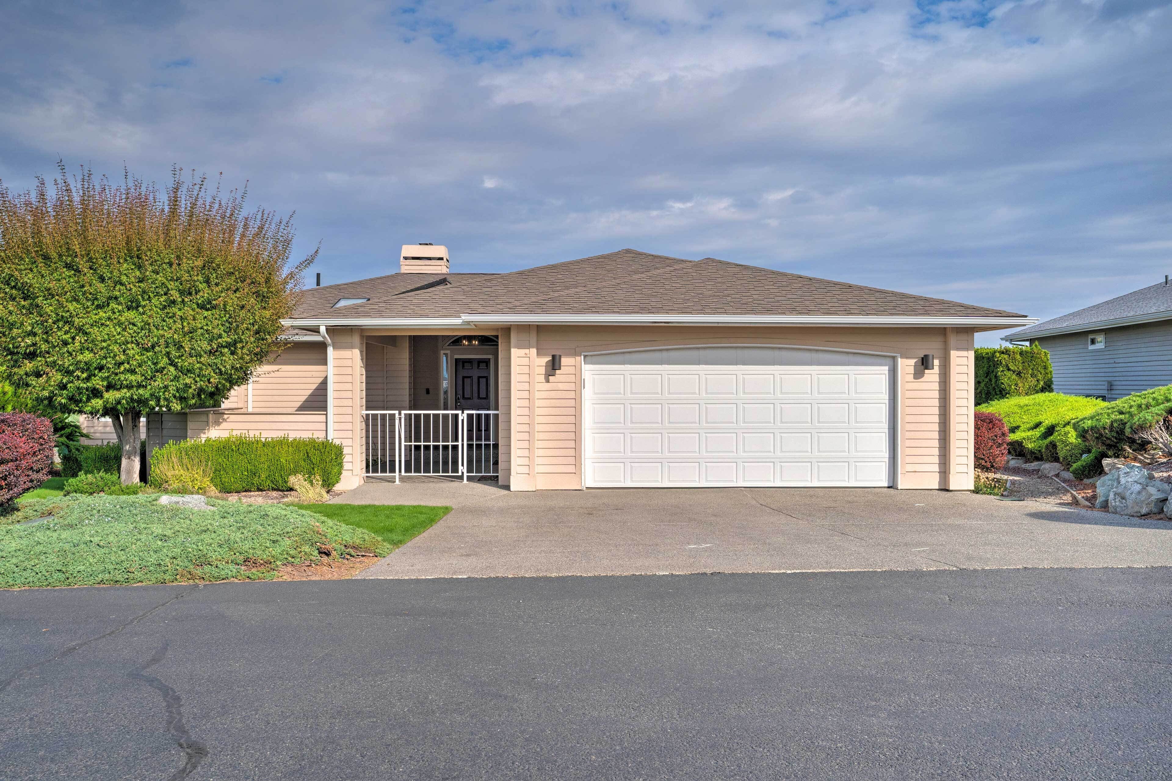A single-story house with a garage, a front yard with a lawn and shrubs, and a clear sky.