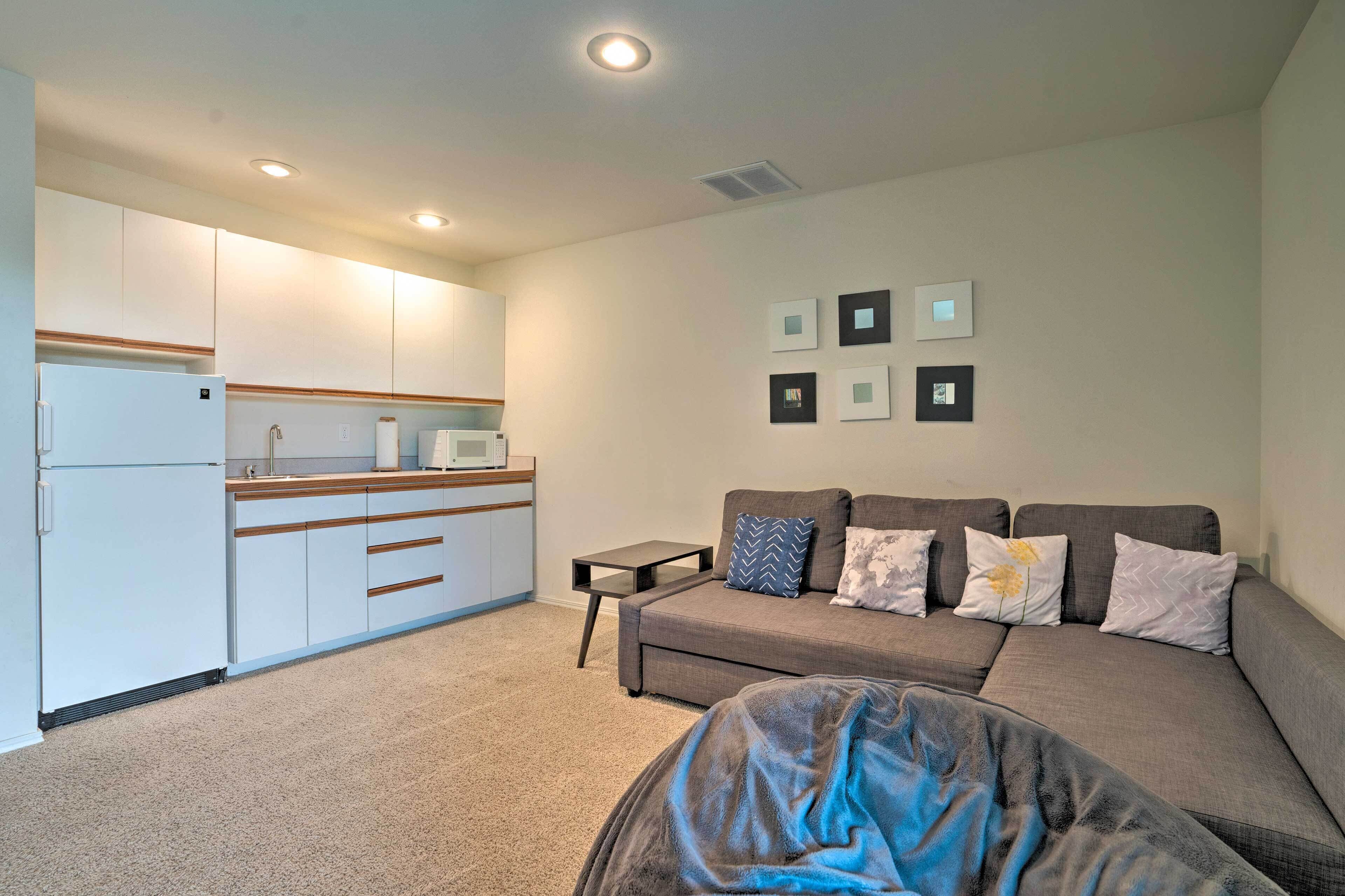 Un espacio habitable compacto con kitchenette, un conjunto de sofás y una pequeña mesa.