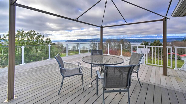 Eine überdachte Terrasse mit einem runden Tisch und Stühlen, mit Blick auf eine malerische Landschaft mit Bergen und einem bewölkten Himmel.
