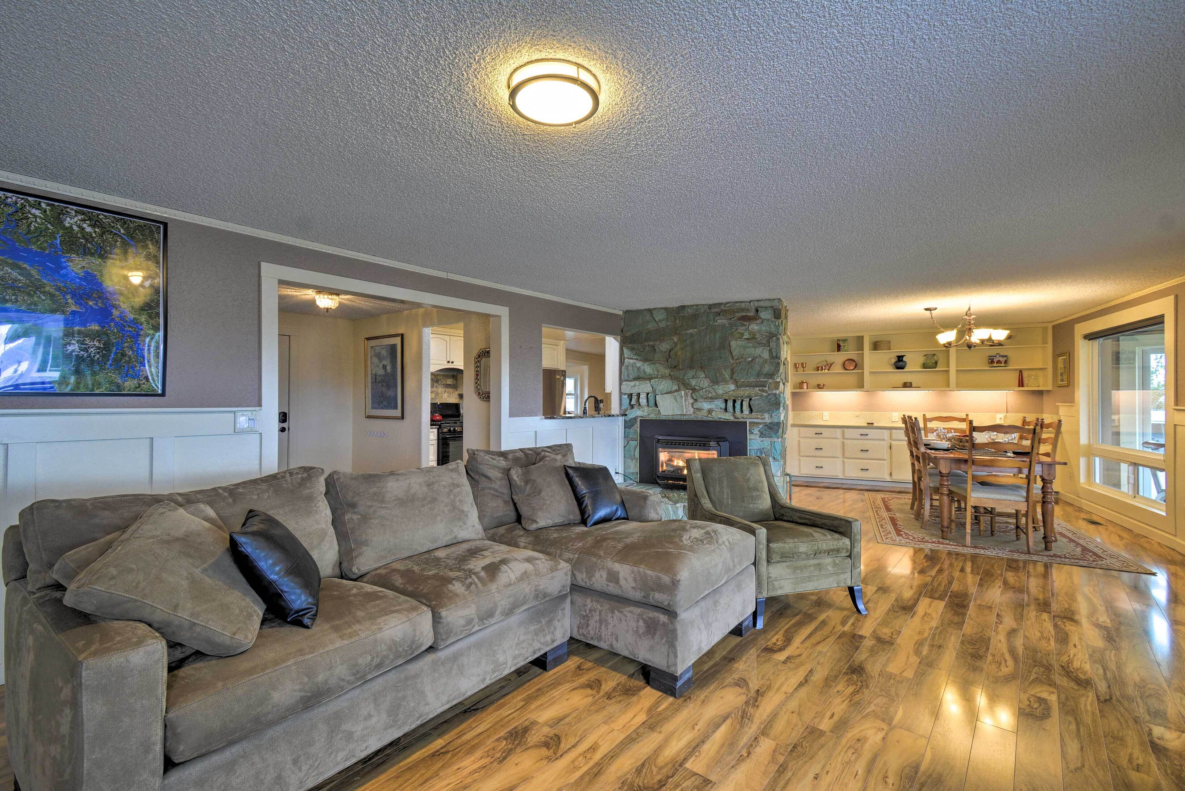 Un salon comprenant un canapé d’angle, une cheminée, un coin repas et une cuisine à l’arrière-plan.