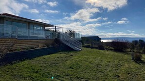 Ein modernes Haus mit einem großen Glasfenster, einer Holzterrasse und Meerblick.