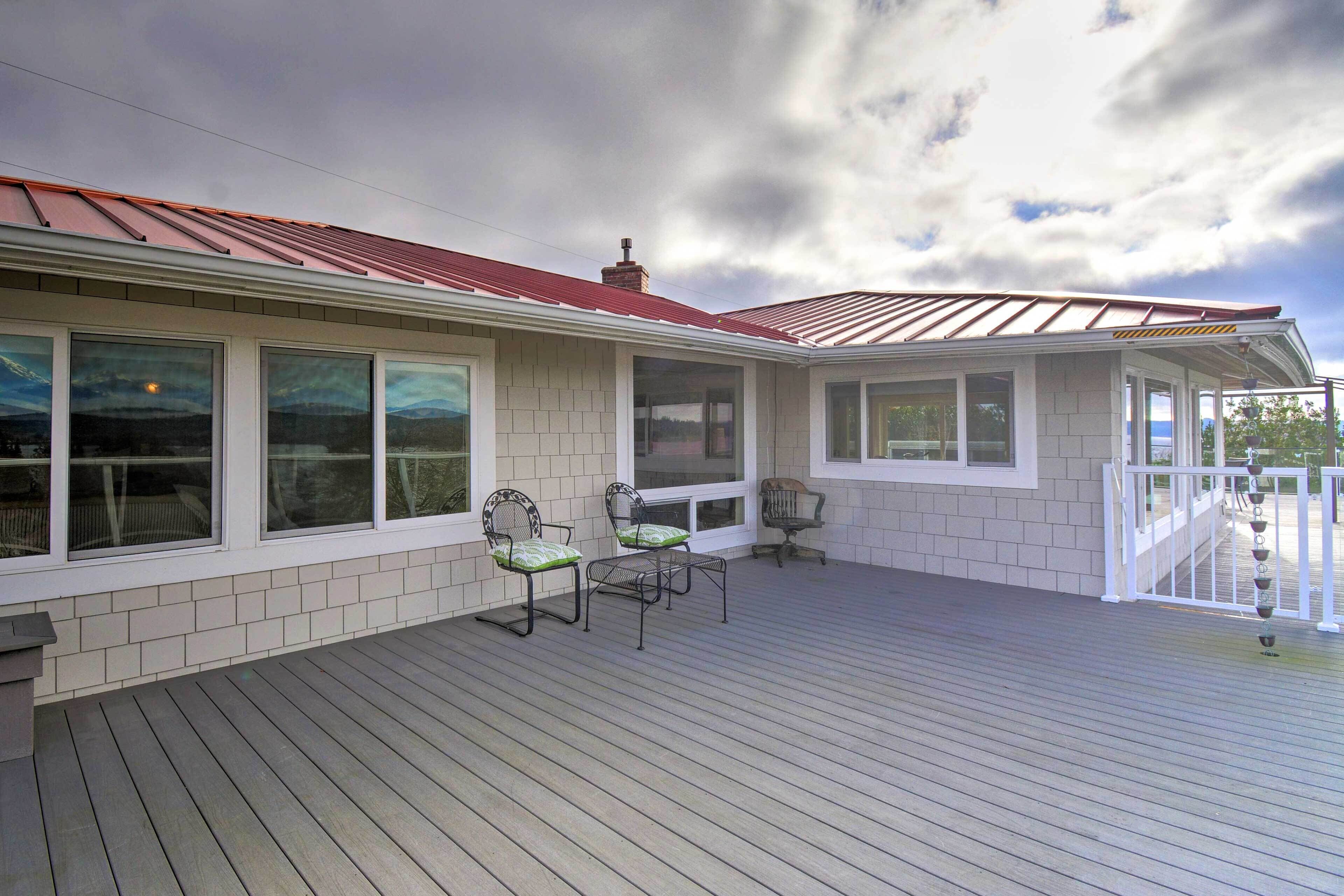 A covered deck with two chairs and a table, a white exterior wall, and a red roof.