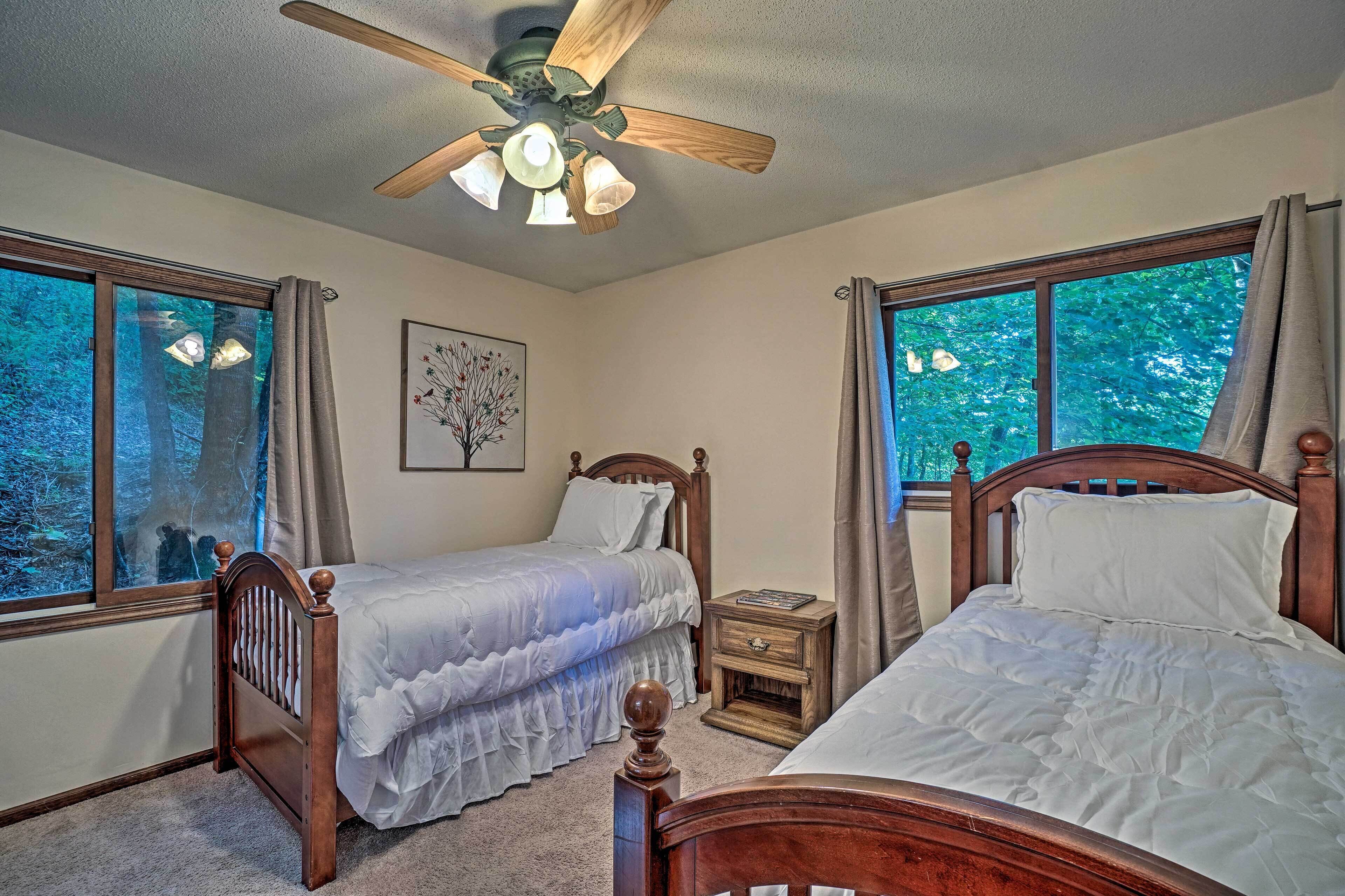 A bedroom with two wooden beds, a ceiling fan, and large windows with curtains.