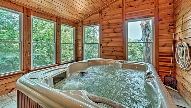 Eine Holzdiele mit Whirlpool, großen Fenstern und Blick auf den Wald.