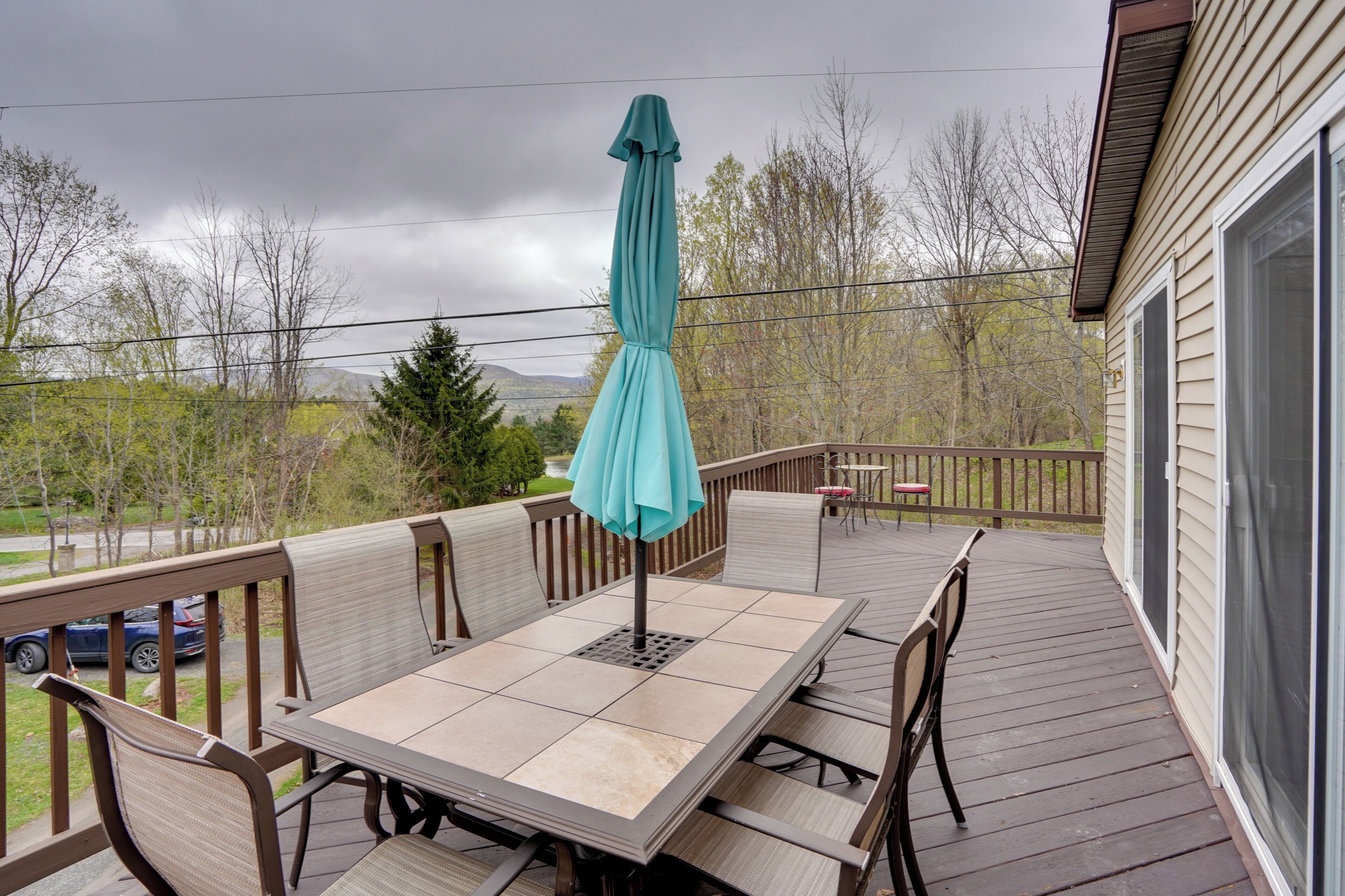 A covered outdoor patio with a table and chairs, a teal umbrella, and a view of trees and a distant mountain.
