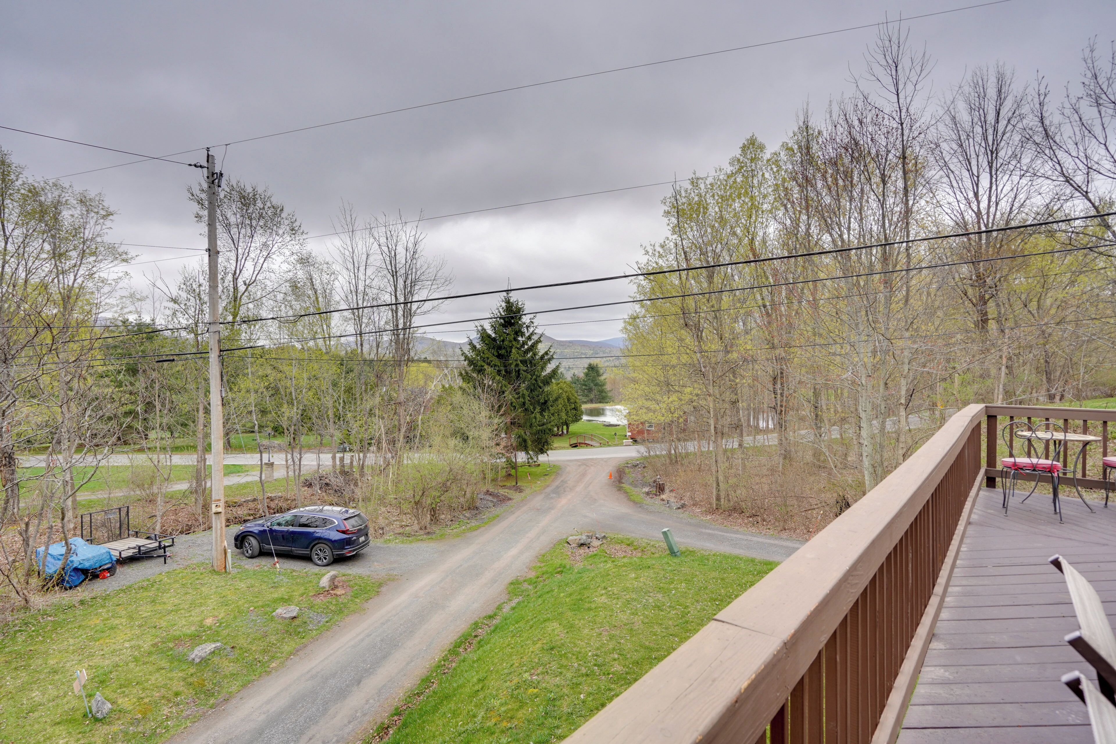 A view from a balcony overlooking a road with a car parked on the side, surrounded by trees and a distant mountain.