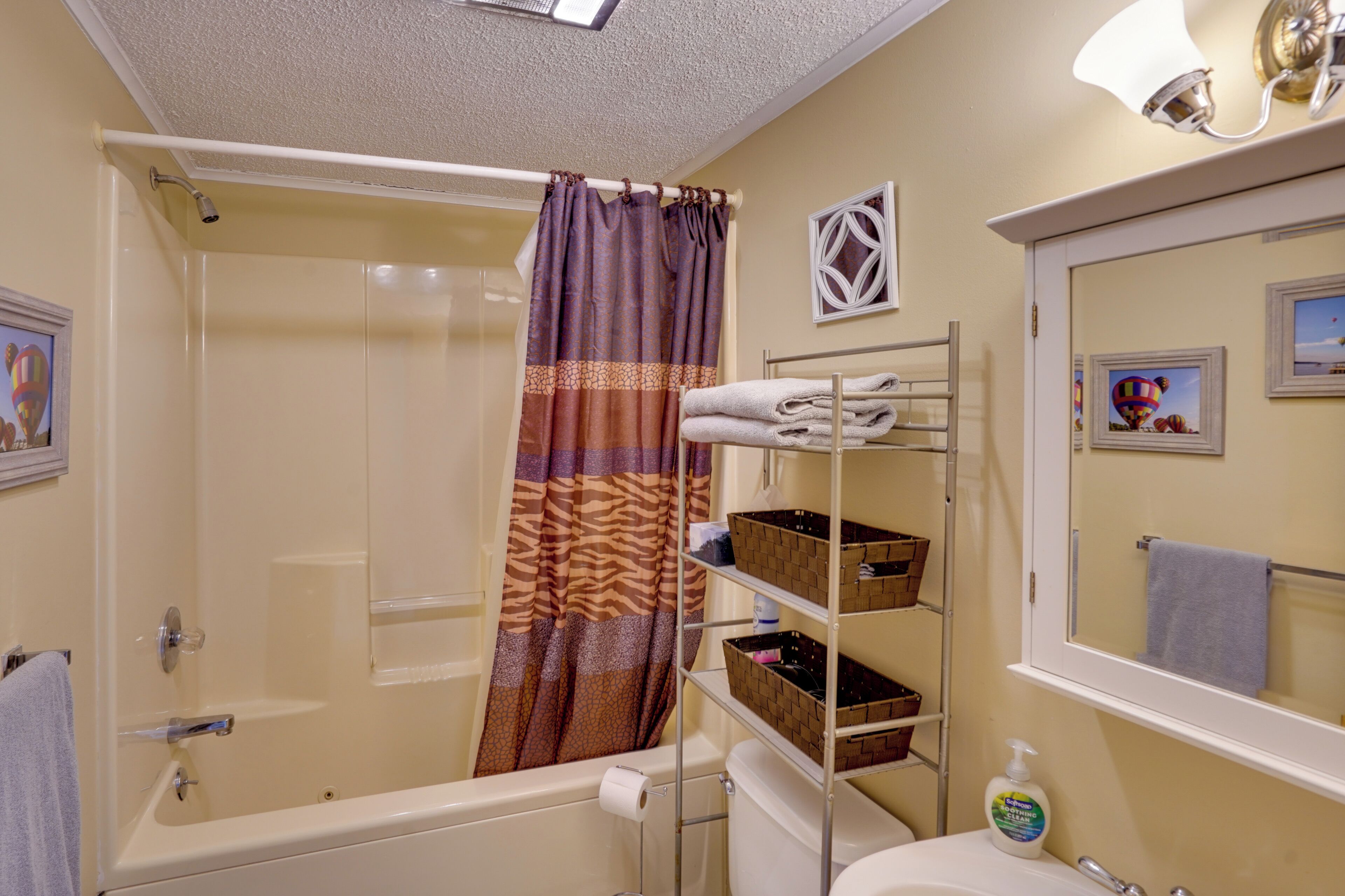 A bathroom with a bathtub, shower curtain, shelves with baskets, a toilet, and a sink with a mirror.
