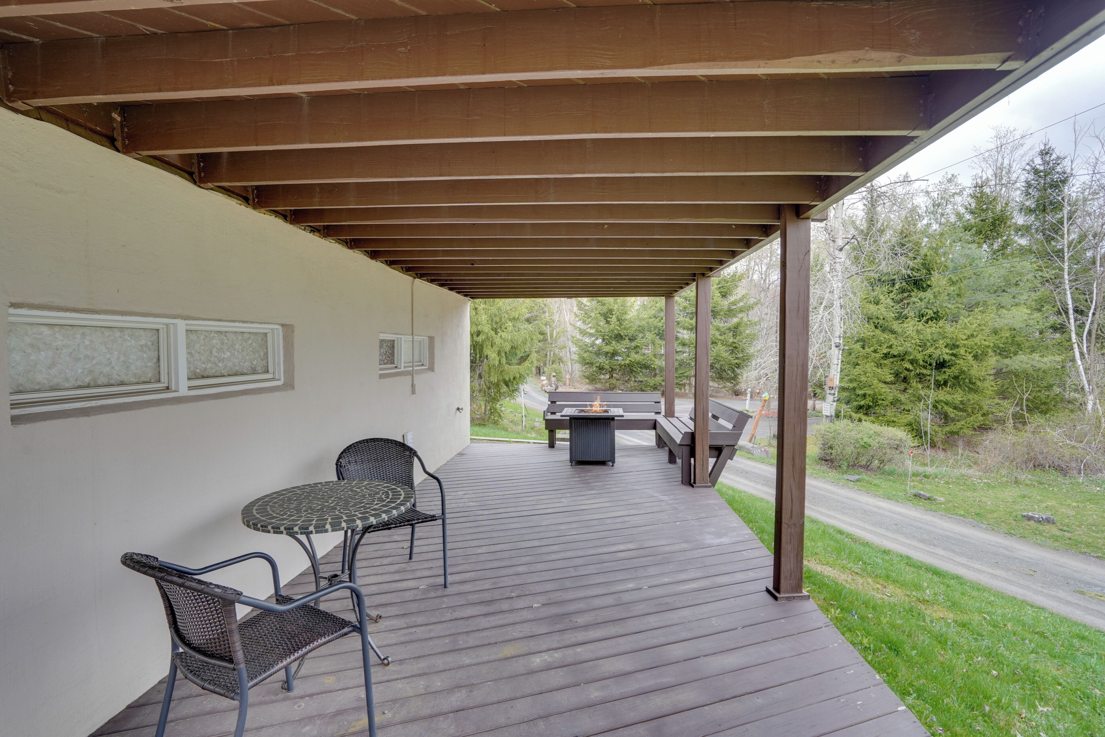 A covered outdoor patio with a table and chairs, a fire pit, and a view of the surrounding forest.