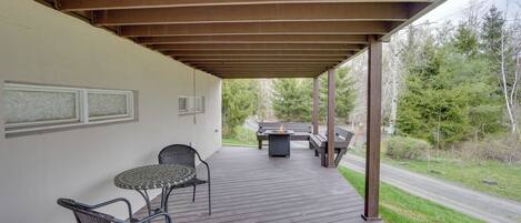 A covered outdoor patio with a table and chairs, a fire pit, and a view of the surrounding forest.
