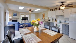 A spacious living area with a dining table, a sofa, and a kitchen with white cabinets and a ceiling fan.