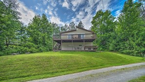A two-story house with a balcony, surrounded by lush greenery and a gravel path leading to the entrance.