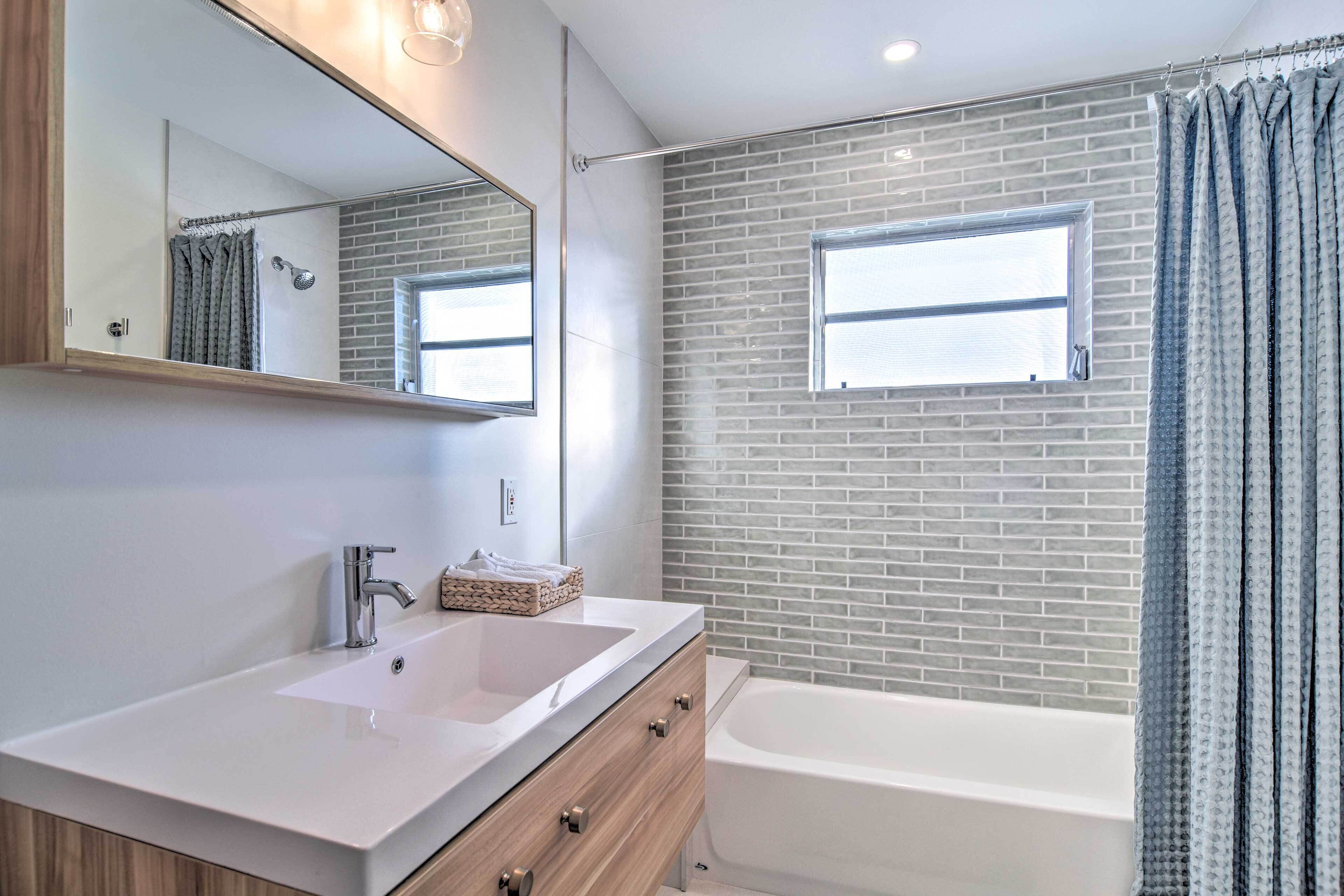 Ein modernes Badezimmer mit einem weißen Waschbecken, einer Holzausstattung, einem großen Spiegel, einem Fenster und einer Badewanne.