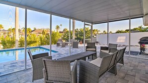 A covered outdoor area with a pool, wicker furniture, and a view of palm trees and houses. - Beach House w/ Pool: 3 Mi to Anna Maria Island! (Bradenton)