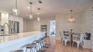 A modern kitchen with a central island, bar stools, pendant lighting, and a dining area with white chairs and a table. - Beach House w/ Pool: 3 Mi to Anna Maria Island! (Bradenton)