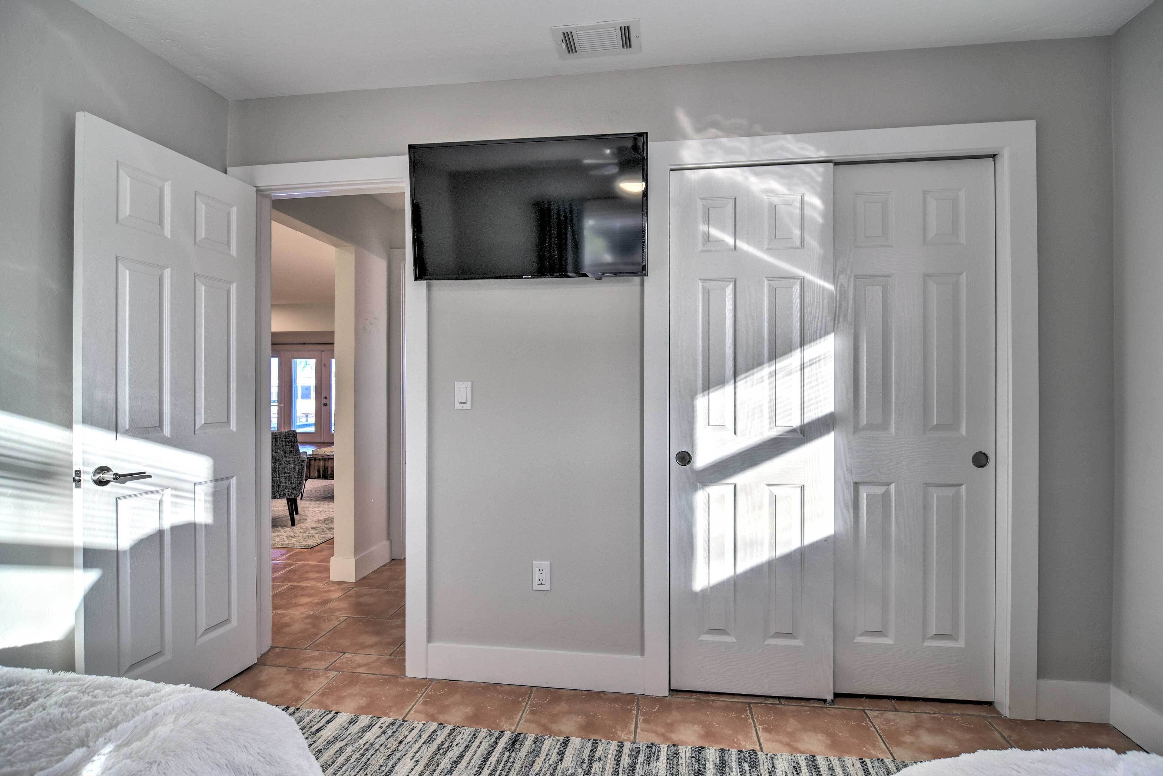 A bedroom with a large bed, a flat-screen TV mounted above a door, and a hallway leading to other rooms.