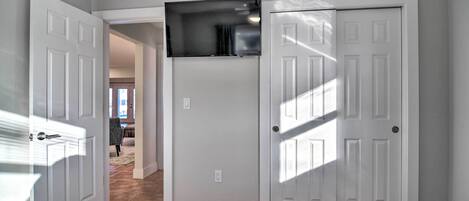 A bedroom with a large bed, a flat-screen TV mounted above a door, and a hallway leading to other rooms.