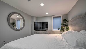 A bedroom with a large bed, a round mirror, a TV, and a window with plants. - 6 Mi to National Mall: Modern DC Apartment! (Washington)