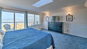 A bedroom with a large bed, a dresser, a television, and a view of the beach through the window. - Eagles View Condo in Ocean Shores w/ 3 Balconies (Ocean Shores)