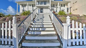 A two-story house with a front porch, a staircase leading to the entrance, and a white picket fence. - Eagles View Condo in Ocean Shores w/ 3 Balconies (Ocean Shores)
