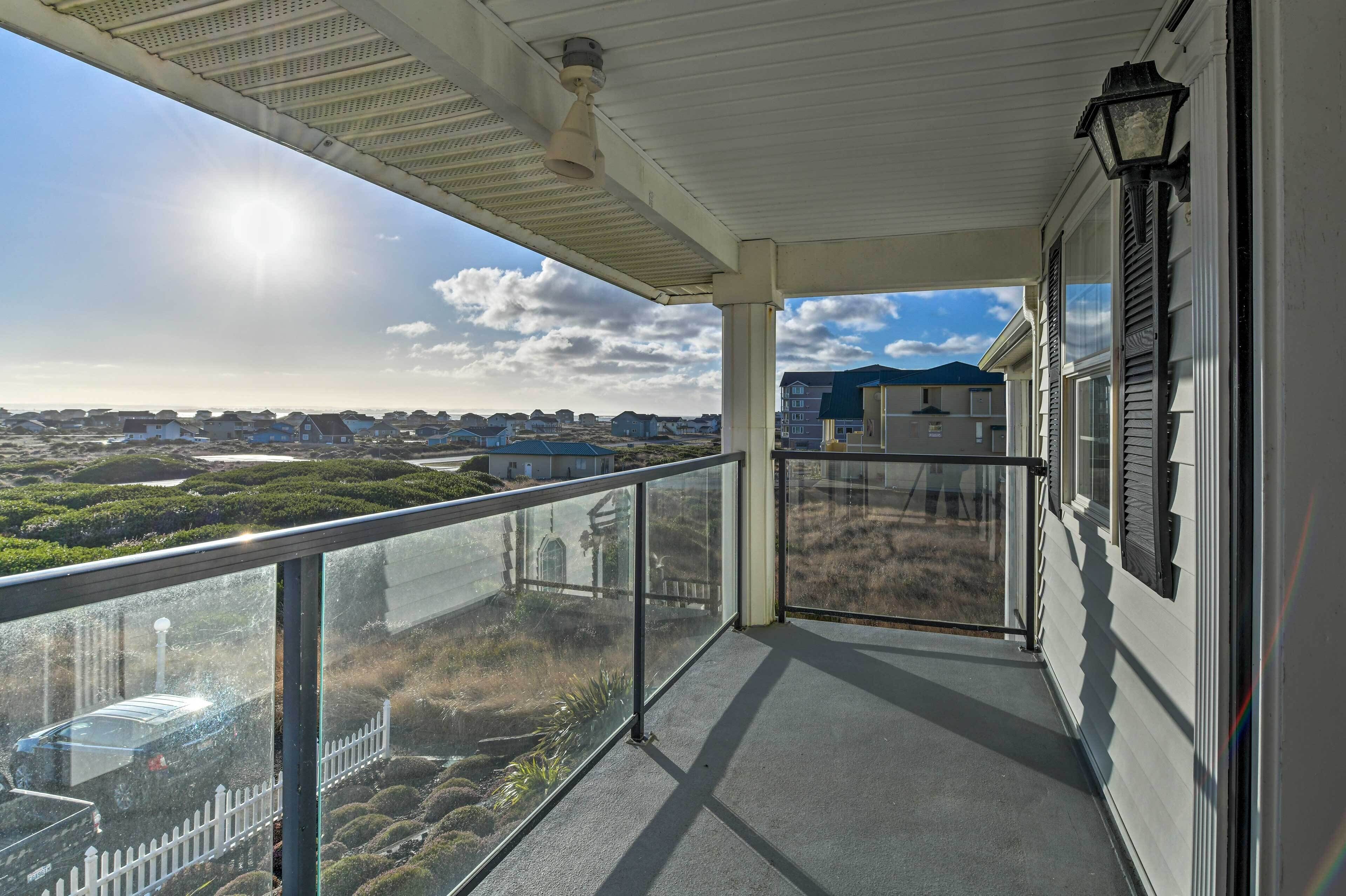 A covered balcony with a glass railing, a view of a residential area, and a clear sky.
