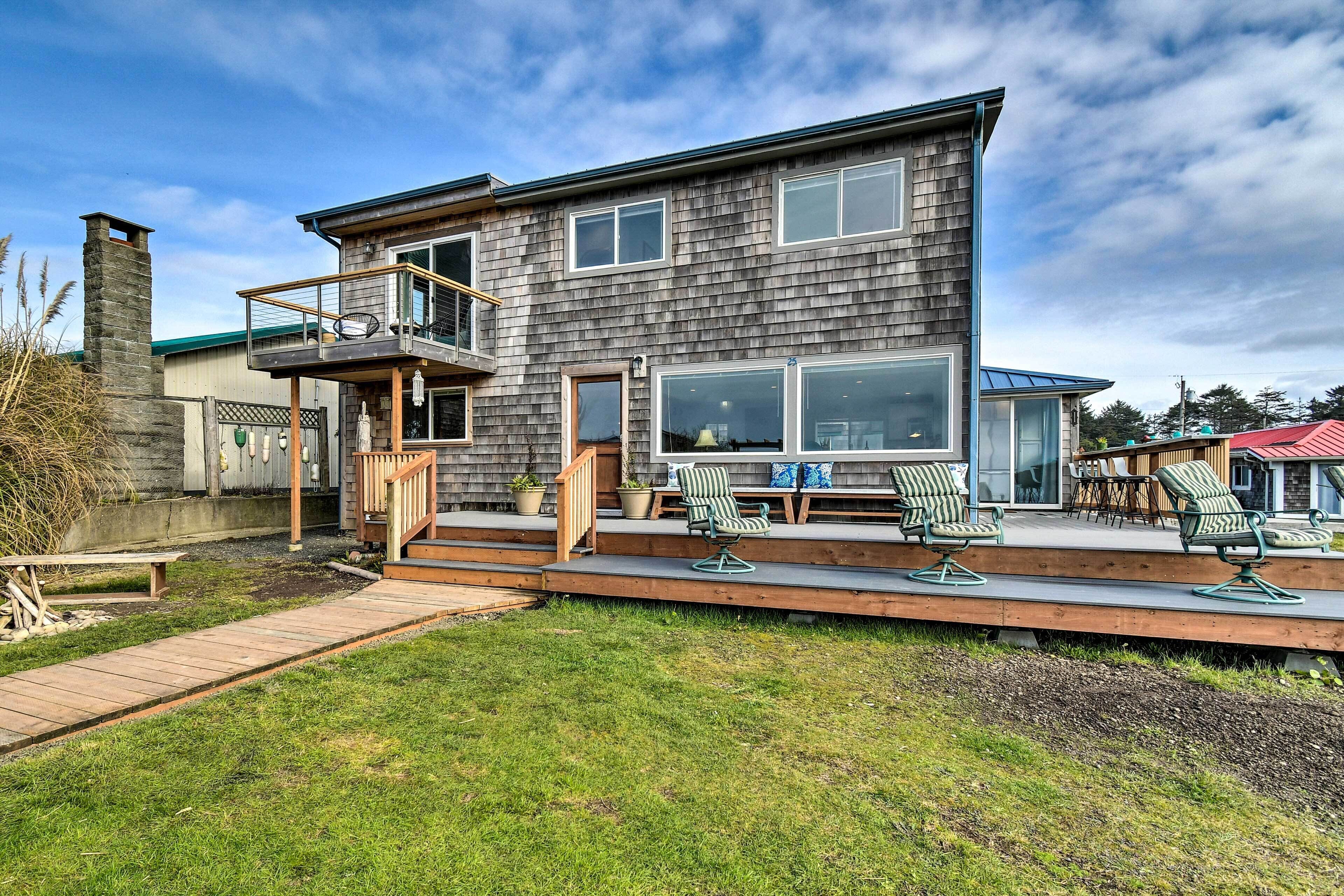 A two-story house with a balcony, a deck with outdoor furniture, and a stone chimney.