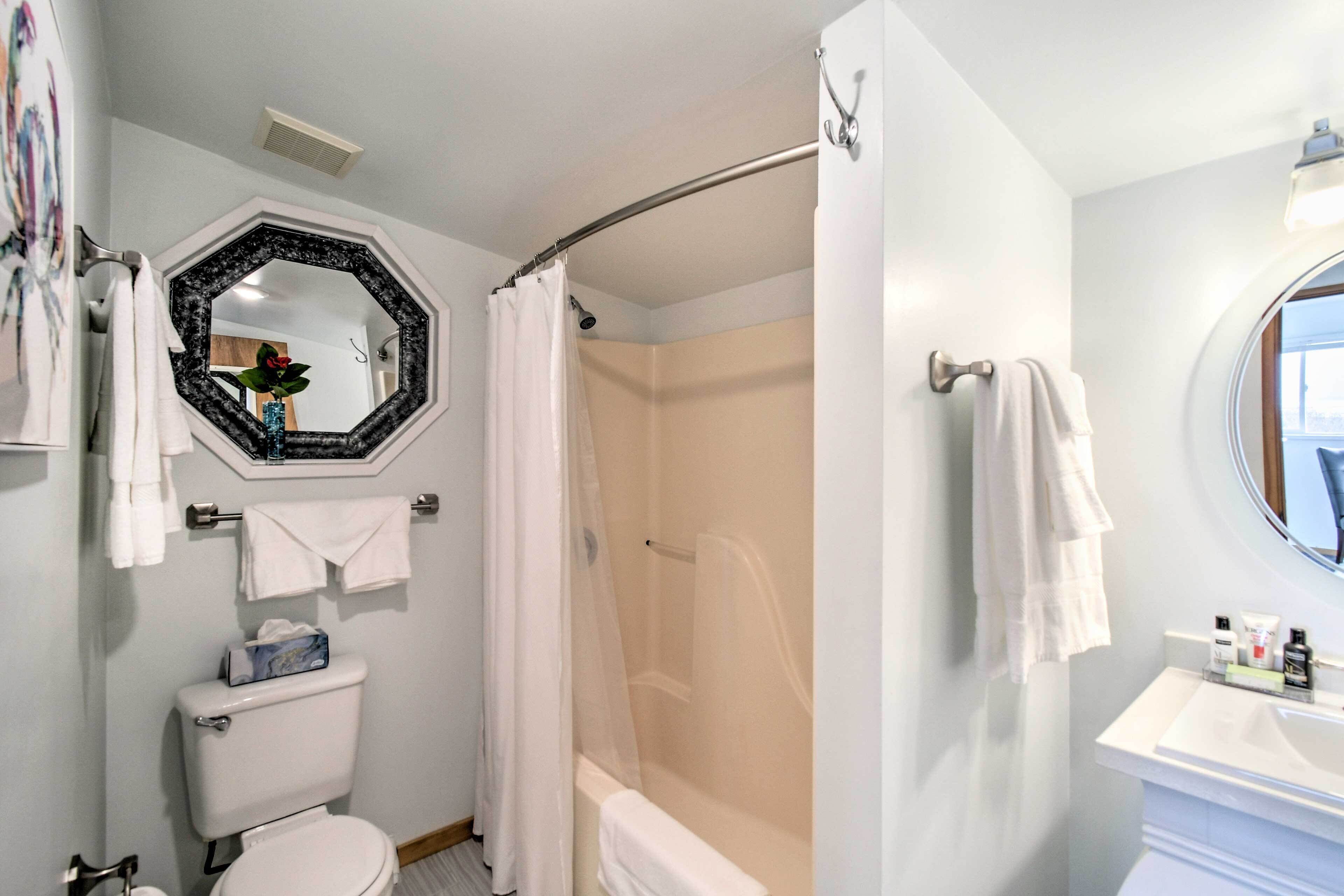 A bathroom with a toilet, a shower with a glass door, a sink with toiletries, and a mirror with a decorative frame.