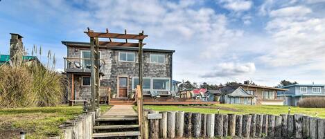 A two-story house with a wooden deck leading to a front door, surrounded by a wooden fence and a grassy yard.