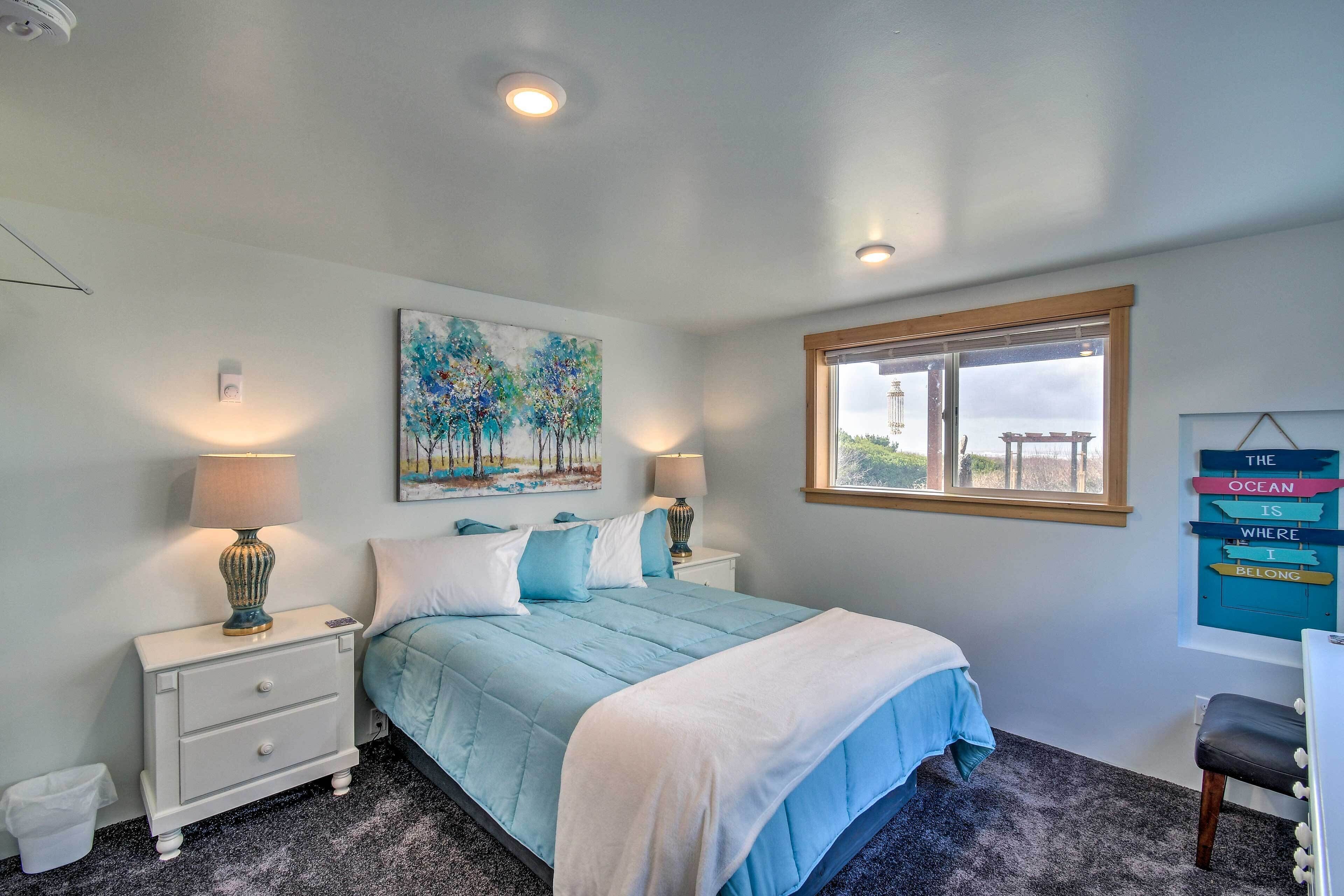 A bedroom with a bed, two bedside tables with lamps, a painting, a window with a view, and a wall-mounted sign.