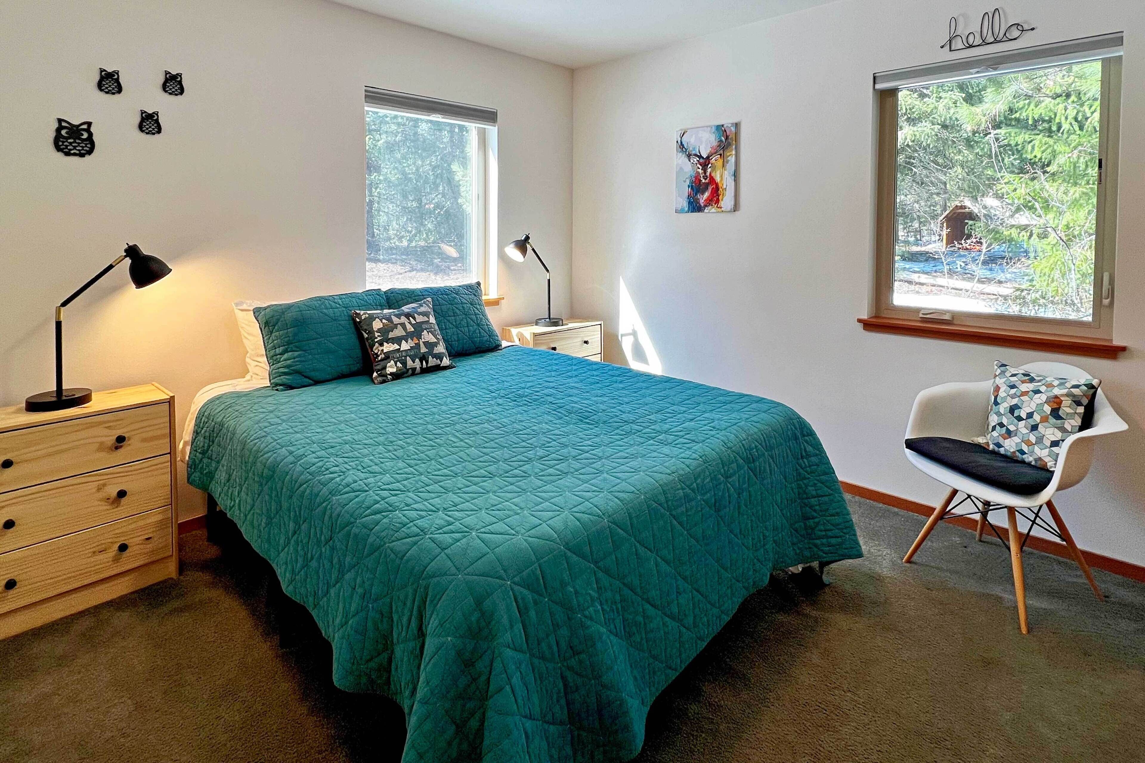 A bedroom with a bed, two bedside tables, a chair, a dresser, and two windows.