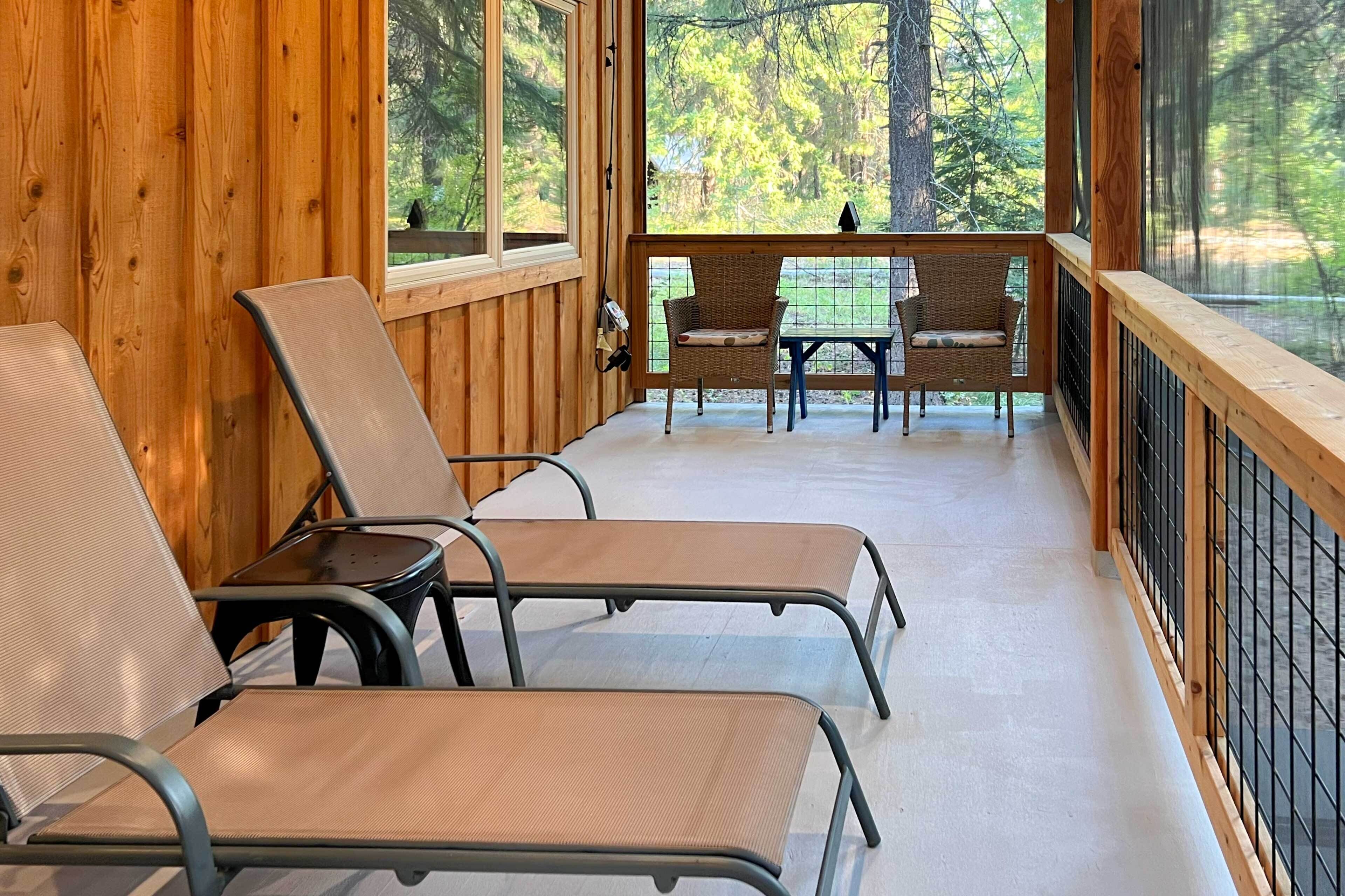 Terraza de madera con sillones y una mesa, con vista a un área boscosa.