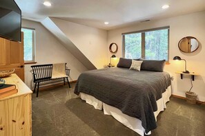 Un dormitorio con una cama grande, dos lámparas de noche, una silla, un armario de madera y una ventana con vistas a árboles.
