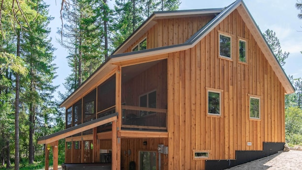 A wooden cabin with a large deck, multiple windows, and a stone foundation. - Modern Beaver Valley Cabin w/ Hot Tub & Games! (Leavenworth)